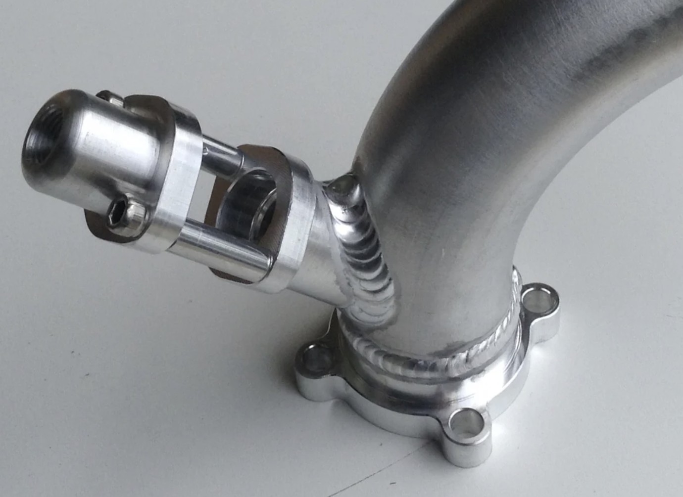 Een metalen injectorhouder gelast aan een gebogen inlaatbuis.